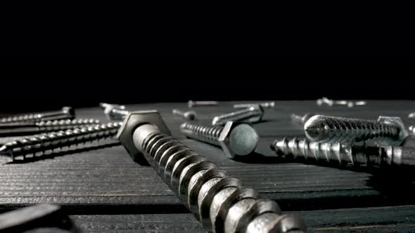 Camera Pans Over Screws Metal Threaded Bolts Fasteners Lying on Table on Black Background