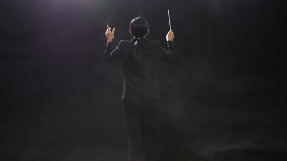 Back View Of Asian Conductor Woman Holding A Baton And Showing Gesture Quickly In The Black Studio