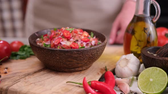 Woman Puts Nacho Chip Into Salsa Dip Sauce in Wooden Bowl