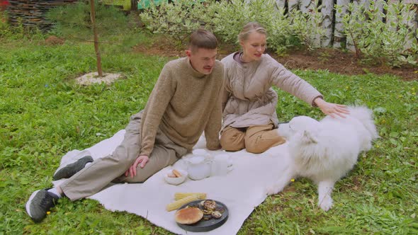 At a Picnic in the Yard of Her Dacha, a Woman Strokes a Dog,a Man Sits Next To Her on a Blanket