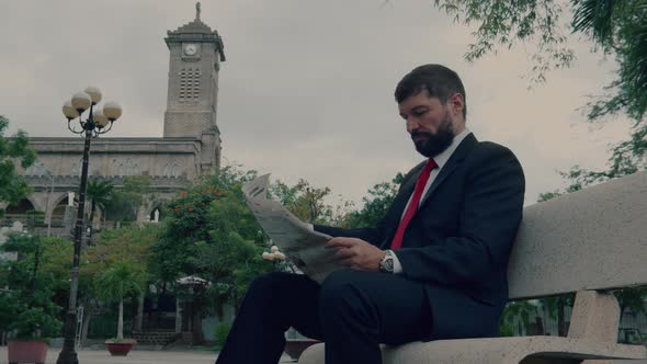 Businessman Senior in an Expensive Suit with a Beautiful Beard in Grey Jacket Sits on Bench in the