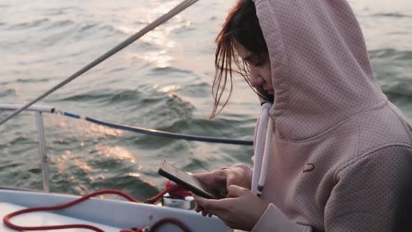 Beautiful Young Woman with a Phone in a Sweater Rides a Private Yacht. Woman on a Yacht Posing