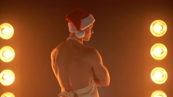 Seductive Muscular Guy in Apron and Santa Hat Going Forward Turning to Camera and Beckoning with