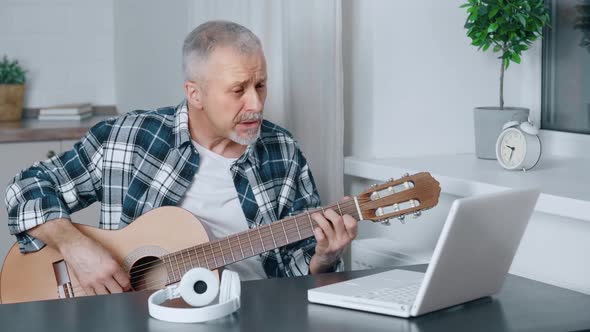 A Man Plays the Guitar Sitting in Front of a Computer at Home