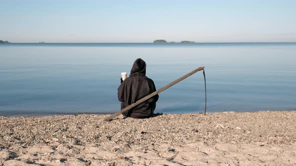 Grim Reaper Sitting By Lake with Cup of Coffee