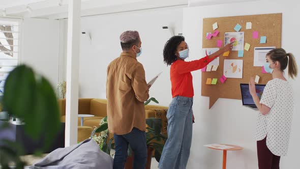 Woman wearing face mask discussing over memo notes with her colleagues at office