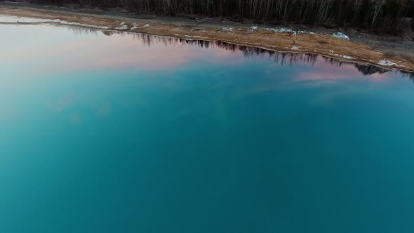 Aerial shot of sky and forest in reflection of water surface, snow lies in Kenai Lake, Alaska, USA