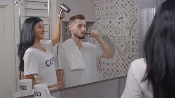 Man Brushing Teeth while Wife Drying His Hair