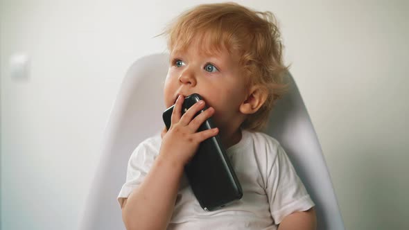 Little Boy Holds Cell Phone Near Mouth Sitting on Chair