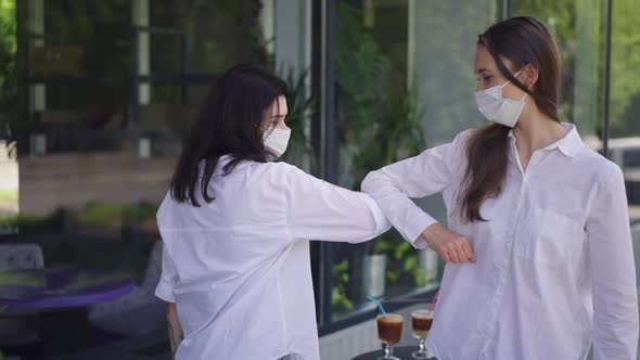 Two Women in Coronavirus Face Masks Touching Elbows in Slow Motion Talking Meeting Outdoors in