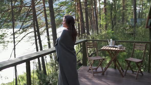 Girl Wrapped in a Plaid on the Balcony in a Mountain House. Attractive Brunette Girl Enjoys Nature