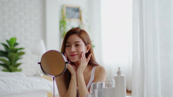 young woman smile and looking in mirror doing skin care touch cheek massage and beauty treatment