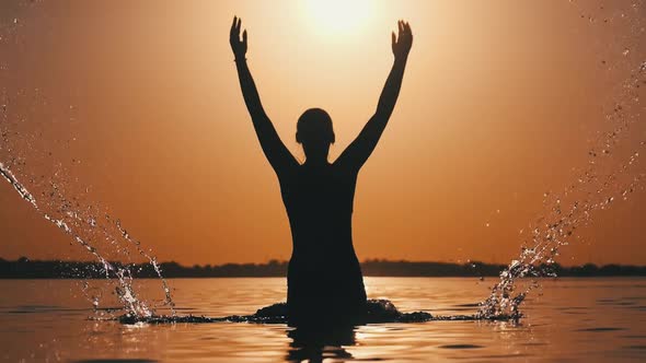 Silhouette of Young Cheerful Woman Splashing River Water at Sunset. Slow Motion