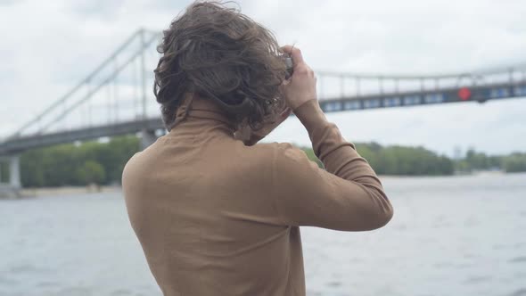 Back View of Brunette Curly-haired Man Taking Photos of Urban Bridge with Retro Camera