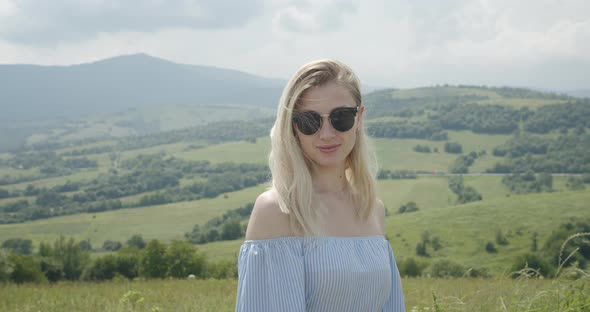 Beautiful Girl in Sunglasses Is Smiling. Sunny Day. Beautiful Mountains in the Background 