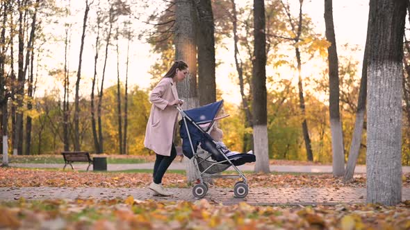 Slow motion of a young woman with a pram and a baby along an alley