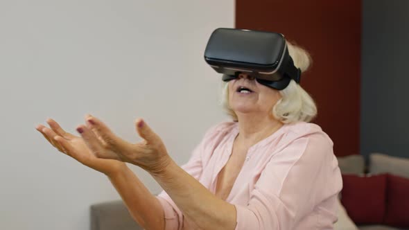 Senior Grandmother Woman in Virtual Headset Glasses Watching Amazing 3D Video in VR Helmet at Home