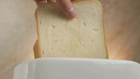 a Man's Hand Loads Two Pieces of White Bread Into a Toaster.