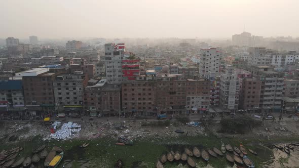 A drone pulls back over the river in Old Dhaka showing the tall buildings and boats going down the r