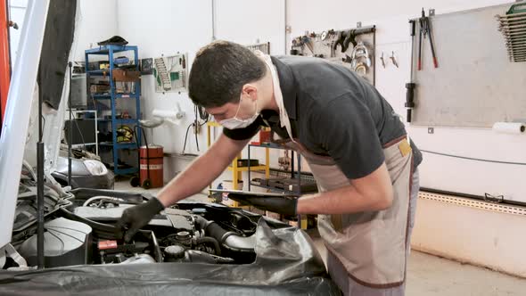 Skilled mechanic wearing protective face mask and gloves in his working environment. Handheld shot.