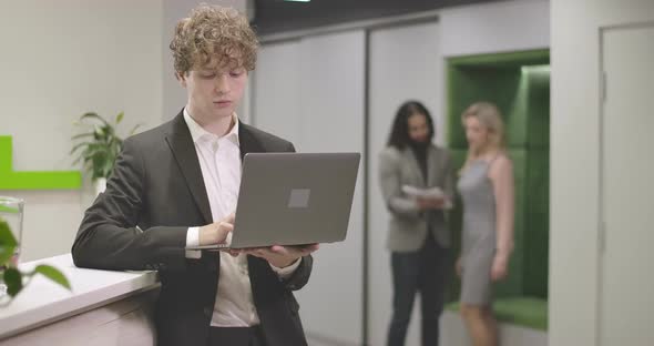 Portrait of Young Caucasian Man Typing on Laptop Keyboard, Looking at Camera and Smiling. Confident