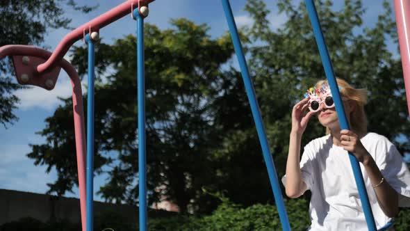 Happy Young Girl in Glasses with Happy Birthdayletteringswings on a Swing in the Park