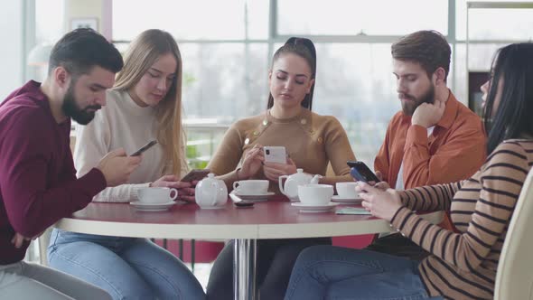 Portrait of Five Bored Caucasian People Sitting in Cafe and Using Smartphones, Young Indifferent Men