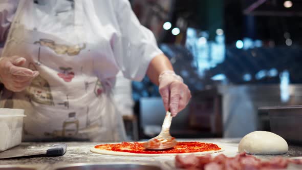 Chef In White Clothes Preparing Pizza Spreading Red Sauce For Pizza Spreading Dough With Metal Spoon