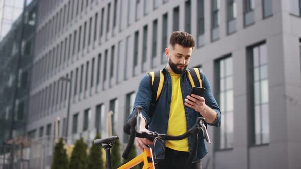 The Food Delivery Guy is Standing and Looking at the Smartphone