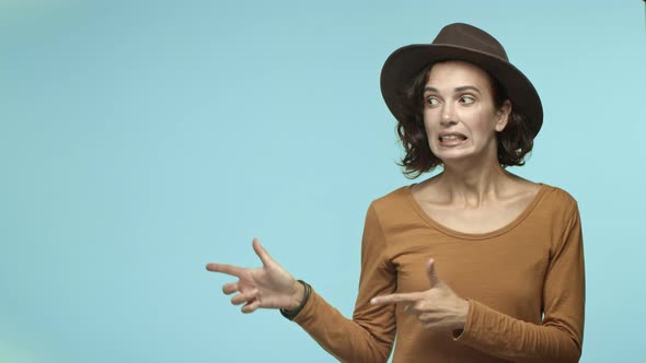 Attractive Woman in Hipster Hat and Casual Brown Blouse Pointing Fingers Left at Copy Space with