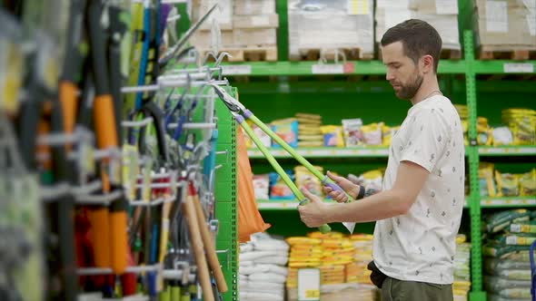 Adult Man is Watching and Trying Pruning Shear in a Hardware Store