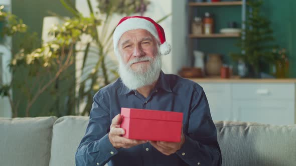 Portrait of a Smiling Elderly Man in a Santa Claus Hat With a Beautiful Box