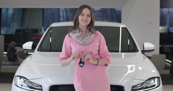 Portrait of Beautiful Young Caucasian Woman Bragging Car Keys in Front of White Automobile in Car