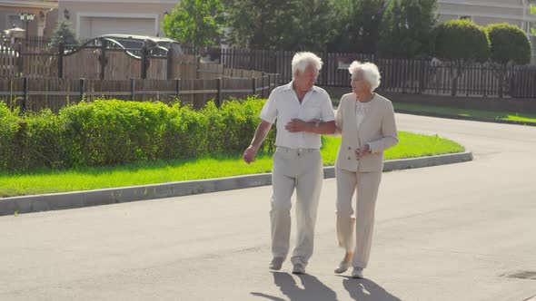 Senior Wife and Husband Speaking and Walking Outdoors on Summer Day