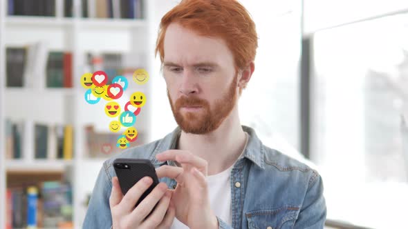 Redhead Beard Designer Using Smartphone, Flying Emojis, Smileys and Likes