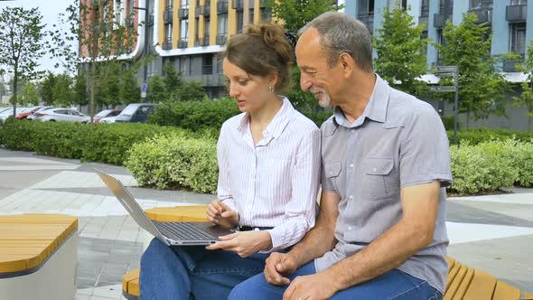 Attractive Young Woman and Senior Man are Using Laptop Sitting on the Bench in Modern Residential