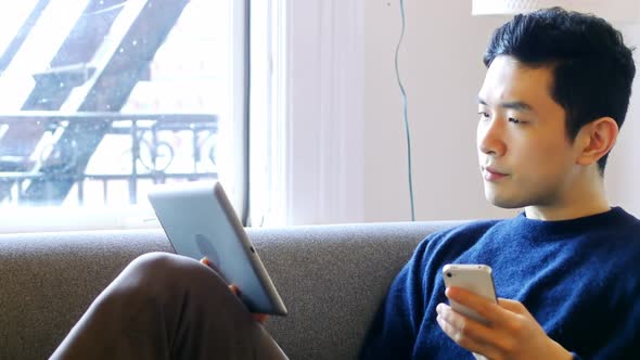 Man using digital tablet and mobile phone in living room 4k