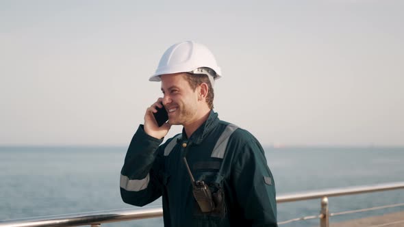 Young Happy Port Worker Talking with Family on Mobile Phone and Smiling While Walking in Seaport