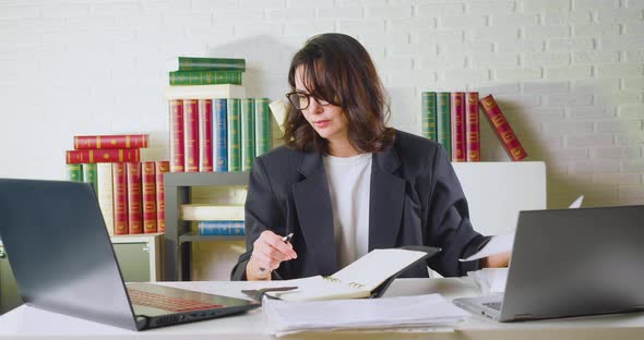 A 40 Year Old Business Woman Checks Reports Tax Forms and Makes Adjustments on a Laptop