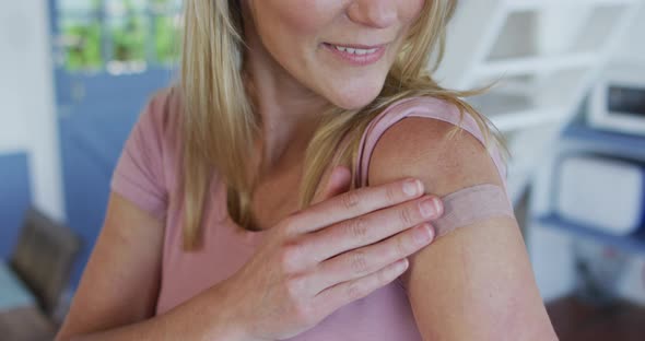 Happy caucasian mature woman showing plaster on arm where she was vaccinated against coronavirus