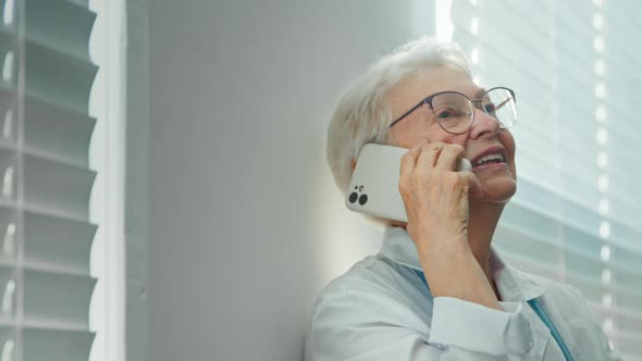 Cheerful skilled lady doctor with grey hair talks on cellphone