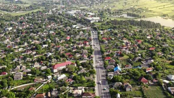 Aerial drone view of a village and road with cars, greenery, lake, Moldova