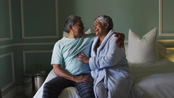 Happy senior mixed race couple sitting on bed embracing