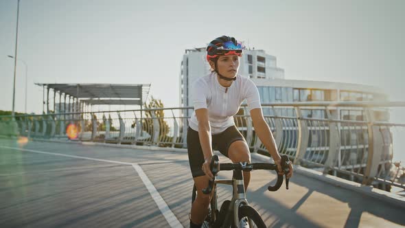 Girl in Sportswear and Protective Helmet is Riding Trekking Bike Downhill Along Bridge Surrounded By