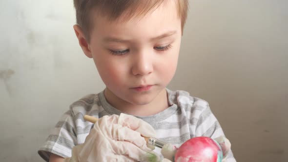 Little Boy Wearing Protective Gloves Draws on an Egg Making an Easter Drawing