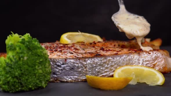 Grilled salmon steak pouring cream sauce and spin on a black background with lemon slice