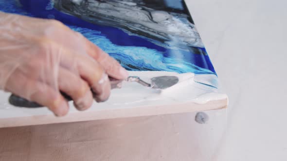 Smears White Epoxy Resin on the Painting with a Spatula on an Abstract Painting