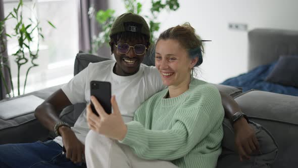 Happy Biracial Couple Sitting on Sofa and Having Video Call on Smartphone