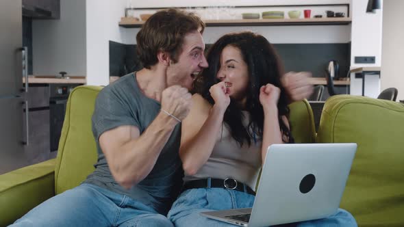 Excited Young Couple Celebrating Success Victory on Laptop While Sitting on Sofa at Home. Lucky