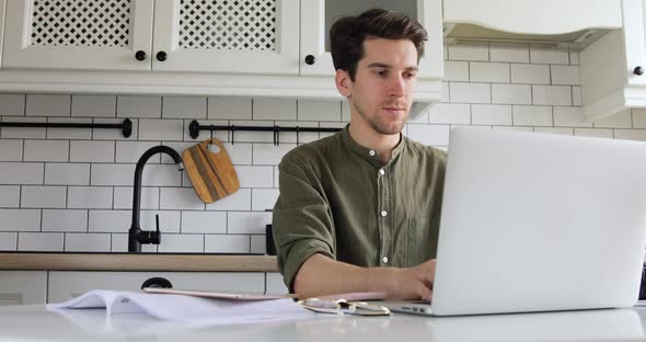 Man sitting in the kitchen and coding html on laptop. IT sphere. Working from home concept